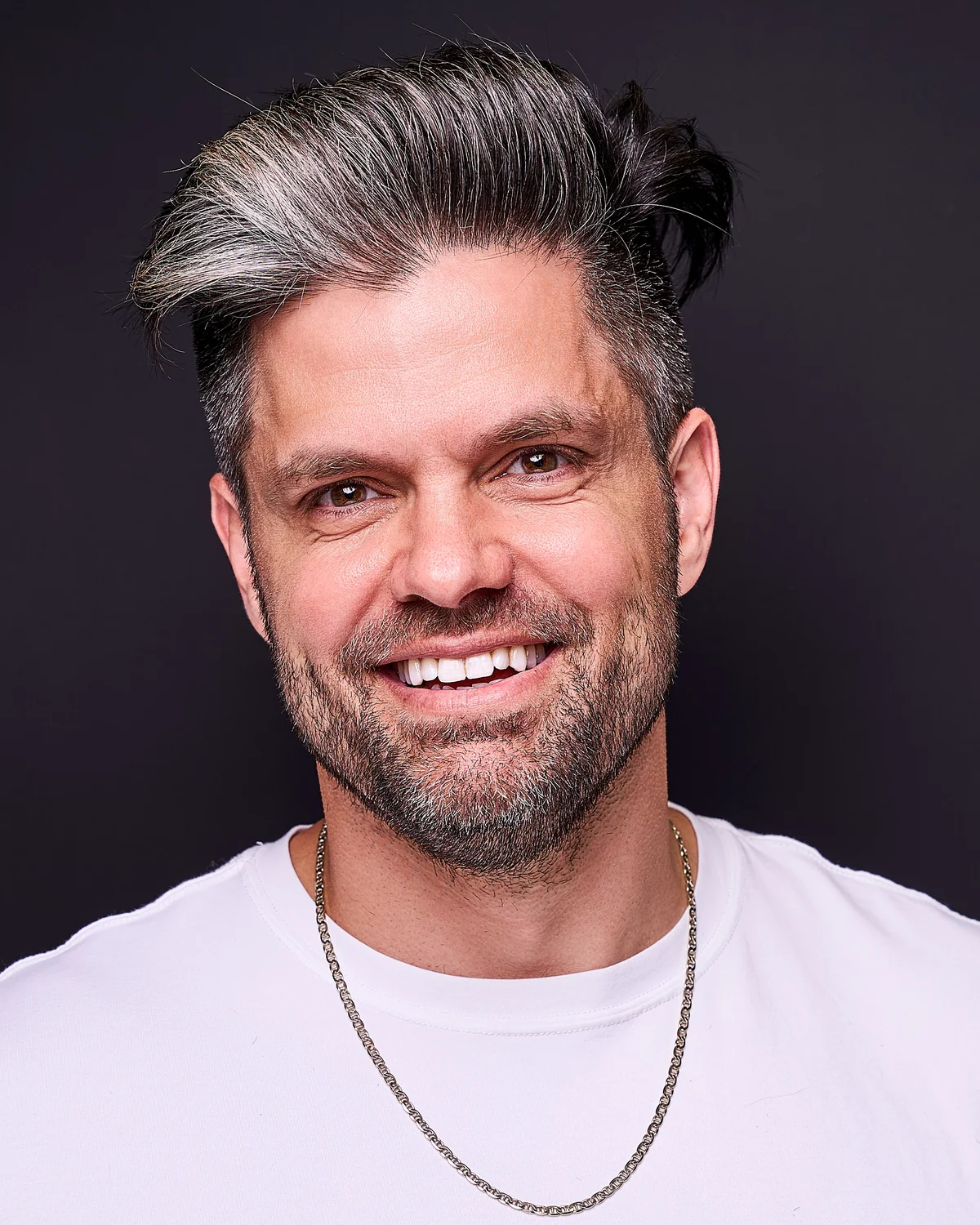 Joshua Albanese, founder of Thought Leader Accelerator, smiling in a white t-shirt against a dark studio backdrop